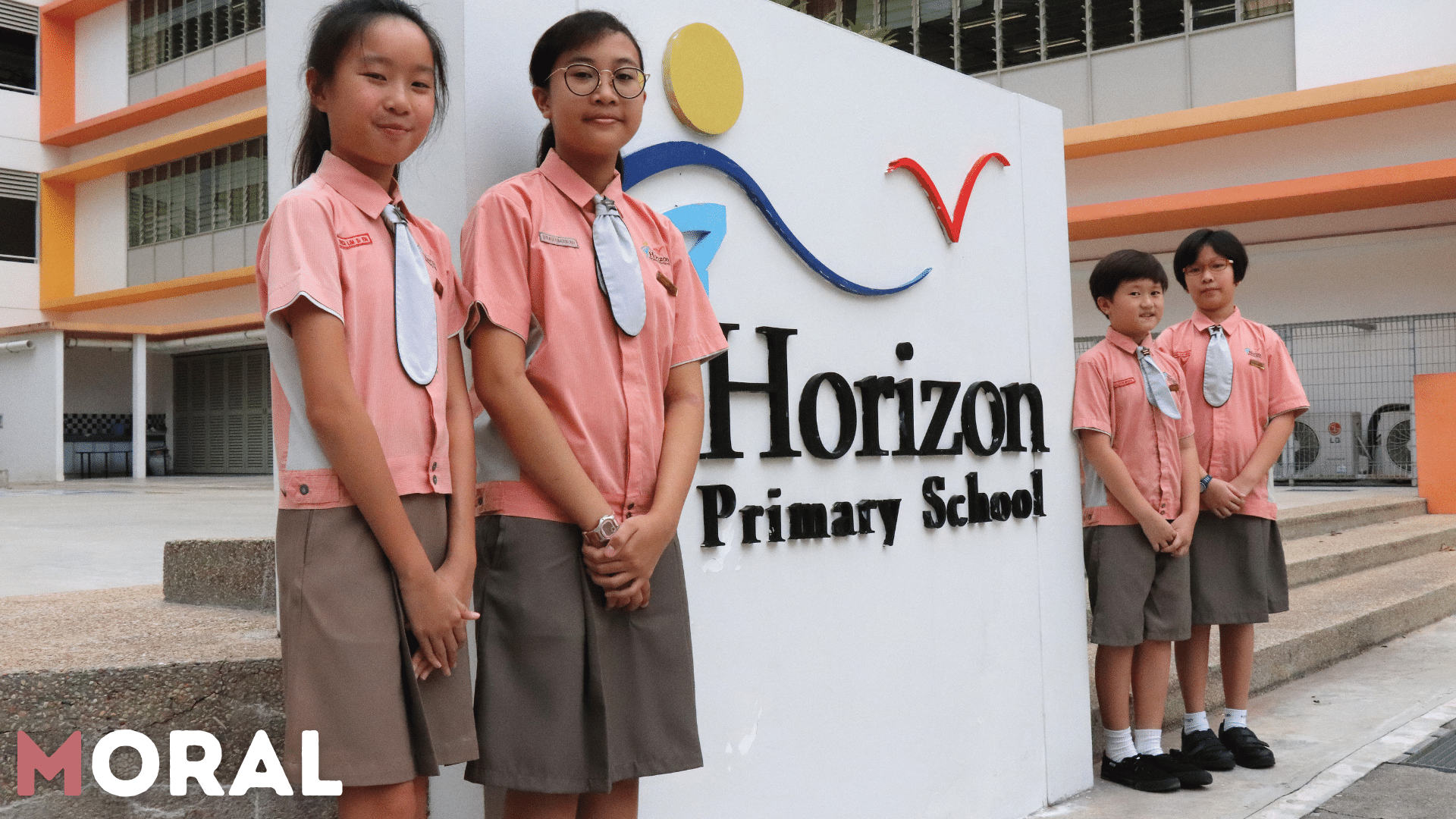 Four students in pink uniforms stand beside the Horizon Primary School sign outside a school building.